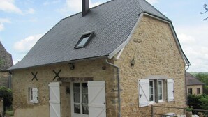 Un bâtiment en pierre avec un toit en pente, deux volets blancs et une petite fenêtre.
