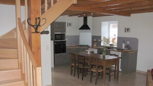 Une cuisine avec une table et des chaises, un escalier et une vue sur le salon.