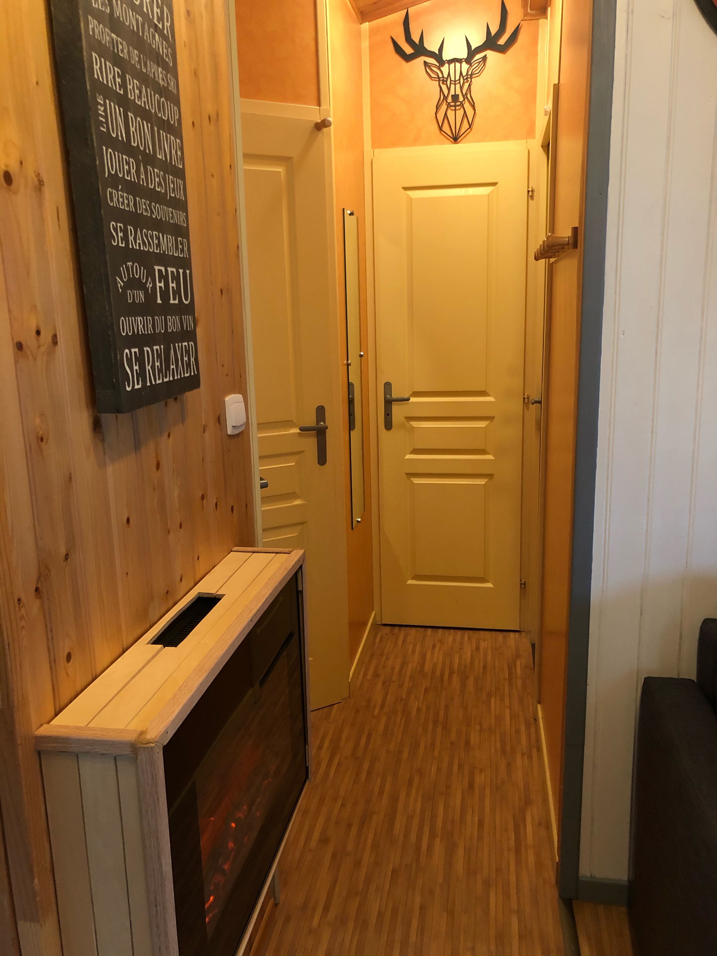 A hallway with wooden walls and a door with a deer head decoration. There is a bench and a wall-mounted sign with text.