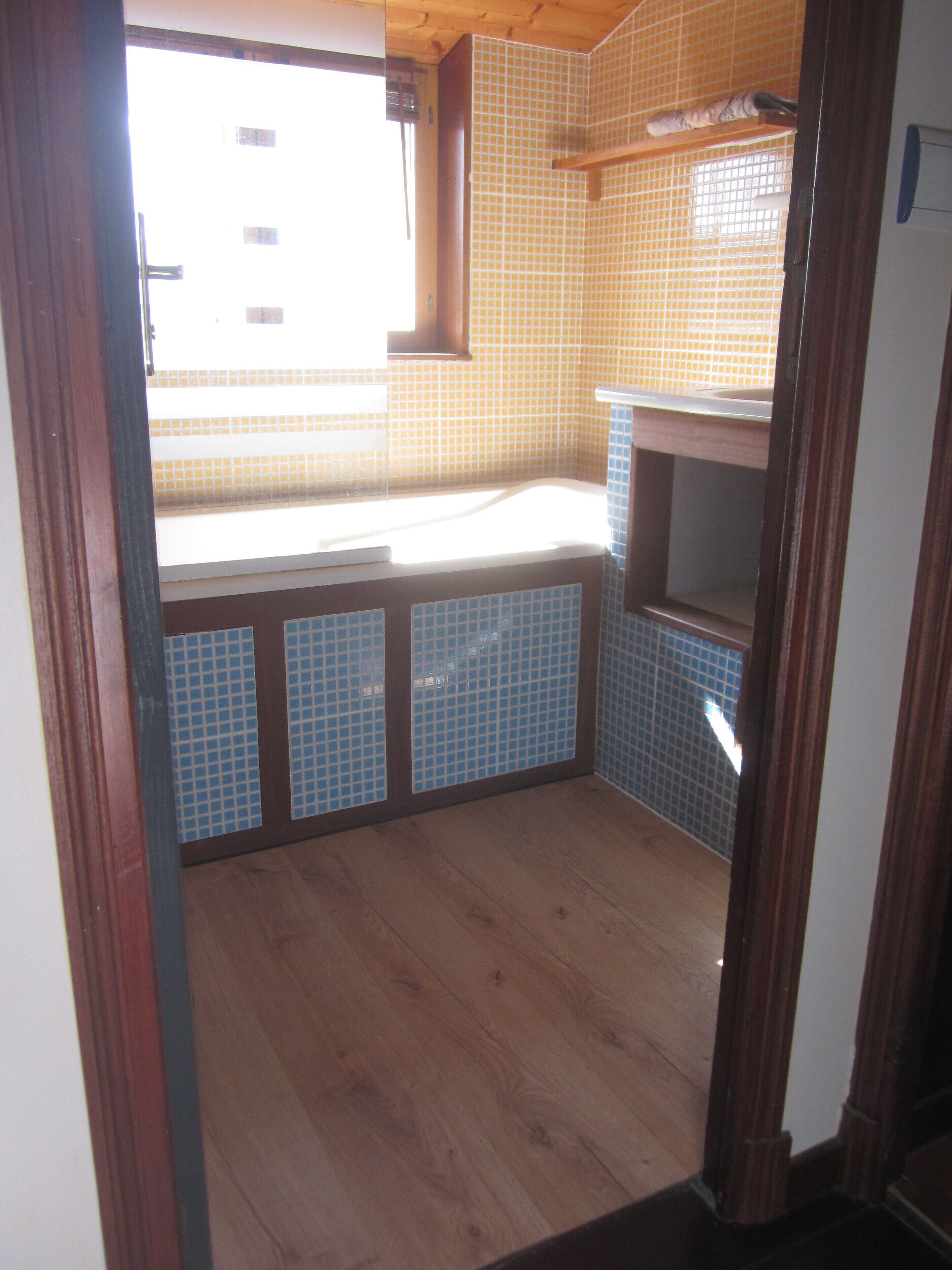 Un baño pequeño y estrecho con suelo de madera, una ventana y paredes de azulejos.