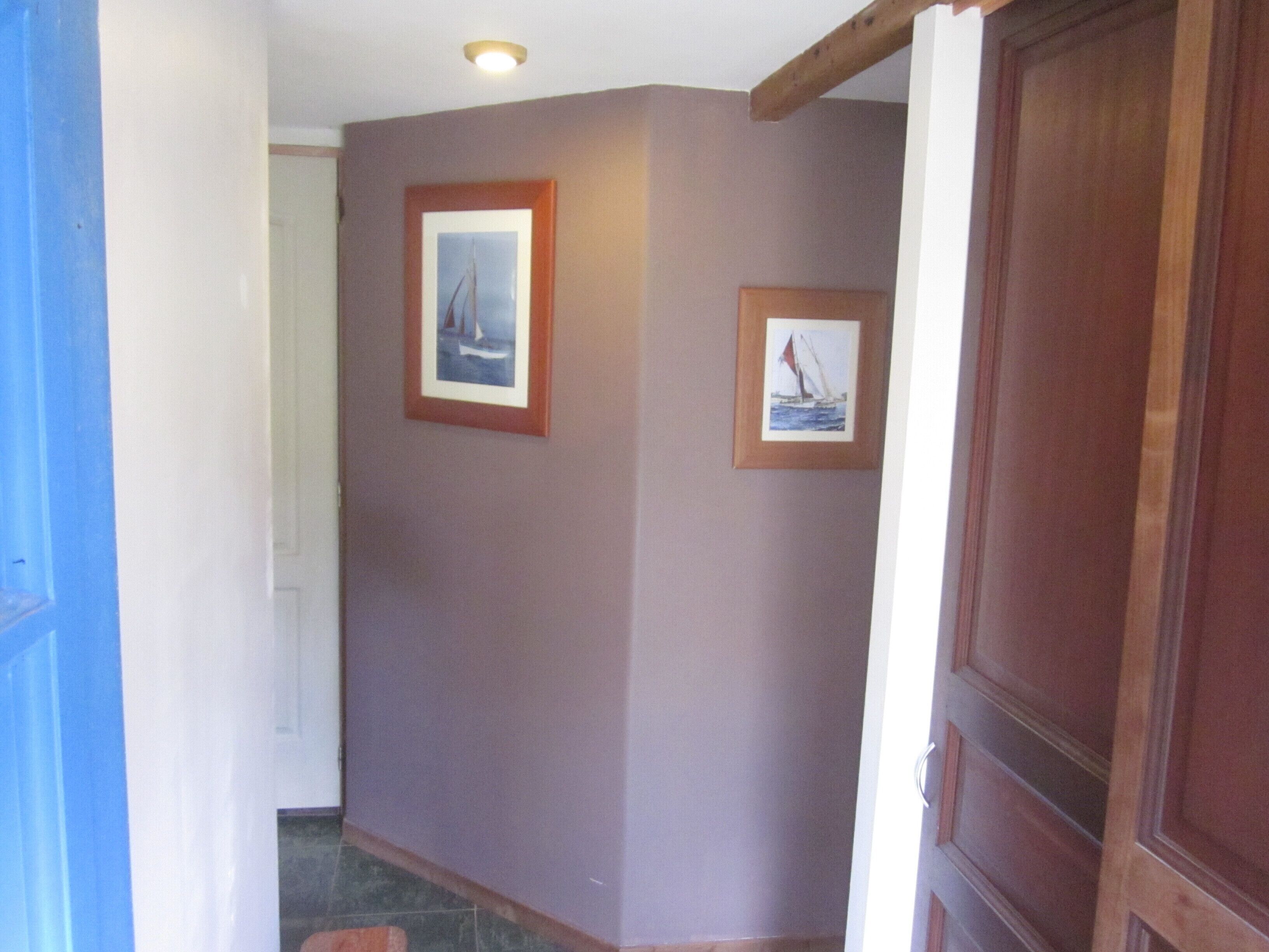 A hallway with a wooden door, a framed picture of a sailboat, and a light fixture on the ceiling.