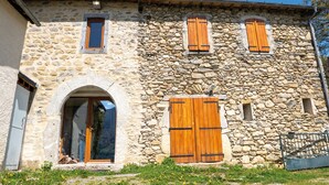 Un bâtiment en pierre avec des volets en bois, une grande porte d’entrée en arc de cercle et un petit escalier menant au toit.