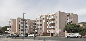 A multi-story hotel with balconies, a parking lot, and a street view. - La Corniche // 2-room apartment 100 meters from the beach (Sète)