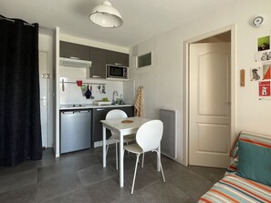 A compact kitchen with a microwave, sink, and dishwasher. There is a dining table with two chairs and a small window. - La Corniche // 2-room apartment 100 meters from the beach (Sète)