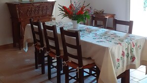 A dining area with a wooden table set for six, surrounded by chairs. There is a floral centerpiece on the table, and a wooden cabinet with a painting above it. - Gîte in an early 18th-century Provencal farmhouse (Roquemaure)