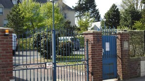 A gated entrance with a blue iron gate, brick walls, and a street visible in the background.