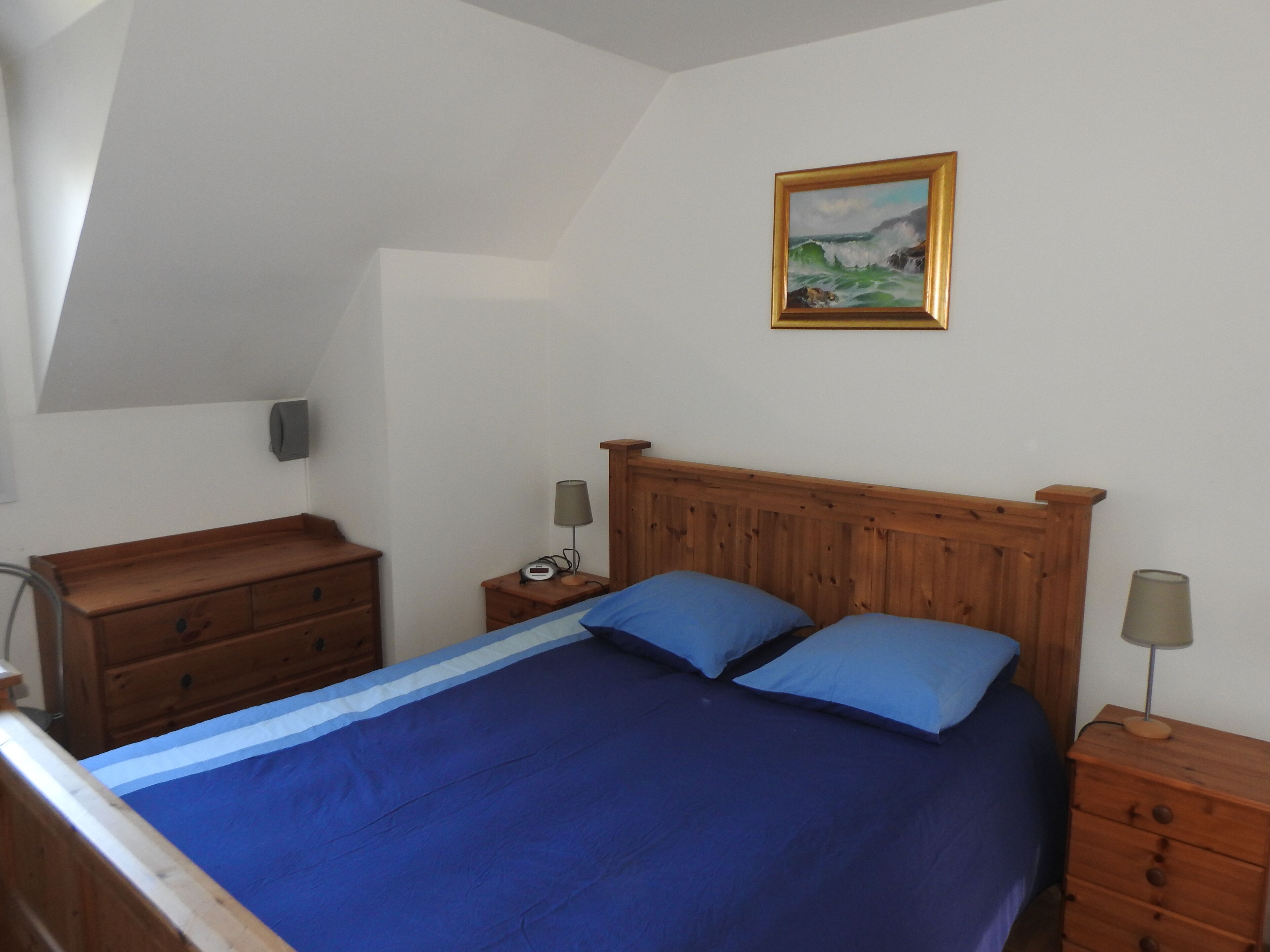 Een slaapkamer met een houten bed, twee nachtkastjes, een dressoir en een schilderij aan de muur.