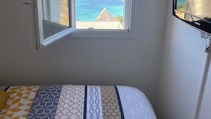 A bedroom with a bed, a window with an open view of the sea, and a wall-mounted TV. - PROMO - Duplex PANORAMIC SEA VIEW, Quiet and close to the BEACH  (Perros-Guirec)