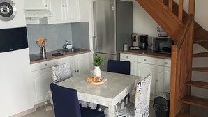 A compact kitchen with white cabinets, a stainless steel refrigerator, a wooden staircase, and a dining table with chairs. - PROMO - Duplex PANORAMIC SEA VIEW, Quiet and close to the BEACH  (Perros-Guirec)