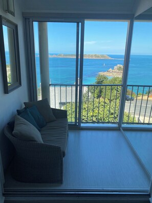 A balcony with a view of the sea, a wicker sofa, and a window with a view of the coastline. - PROMO - Duplex PANORAMIC SEA VIEW, Quiet and close to the BEACH  (Perros-Guirec)