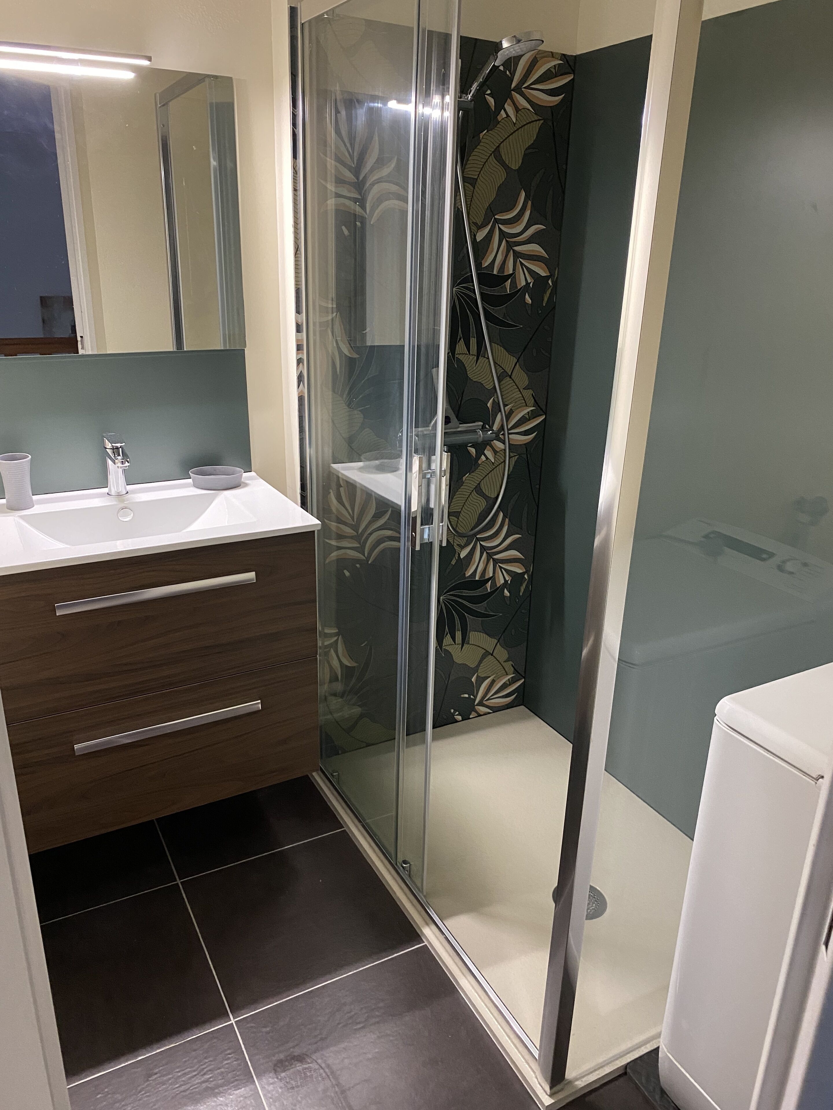 A modern bathroom with a glass shower enclosure, a white sink, and a vanity with drawers.