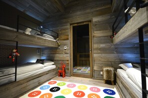 A cozy cabin-style room with bunk beds, a colorful button-patterned rug, and a wooden door.