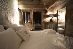 Un dormitorio tipo cabaña de madera con cama, mesita de noche con lámpara, y baño con lavamanos y espejo.