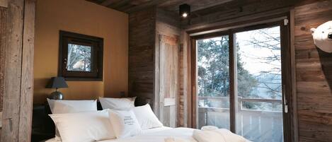 Une chambre à coucher dans une cabane en bois, avec un lit, des oreillers, une table de chevet, une lampe et une fenêtre donnant sur la forêt.