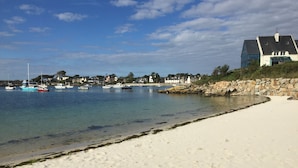 A beach with a sandy shore, a stone wall, and a row of houses in the background.