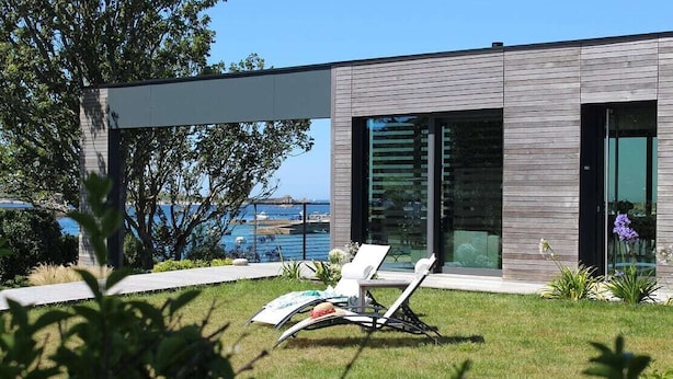 A modern house with a pool, a lawn, and a chair.