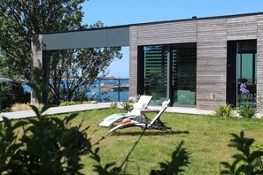 Una casa moderna con piscina, césped y una silla.