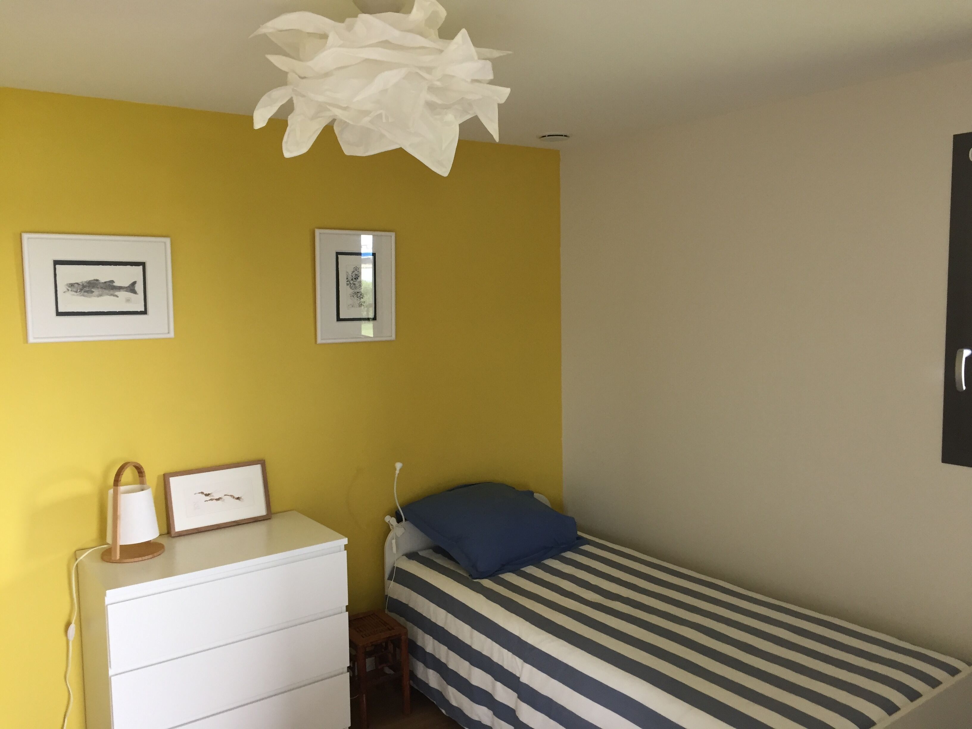Een slaapkamer met een bed, een dressoir, twee ingelijste foto's en een bijzondere witte papieren decoratie aan het plafond.