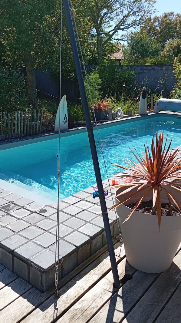 A swimming pool with a wooden deck, surrounded by potted plants and a fence. - Magnifique maison en bord de mer (Labenne)