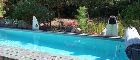 Une piscine dotée d’une terrasse en bois, entourée de verdure et délimitée par une clôture en bois.