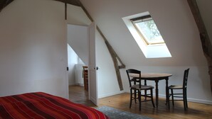 Une pièce avec un plafond en pente, une petite table avec deux chaises, une couvre-lit à rayures rouges et un puits de lumière.