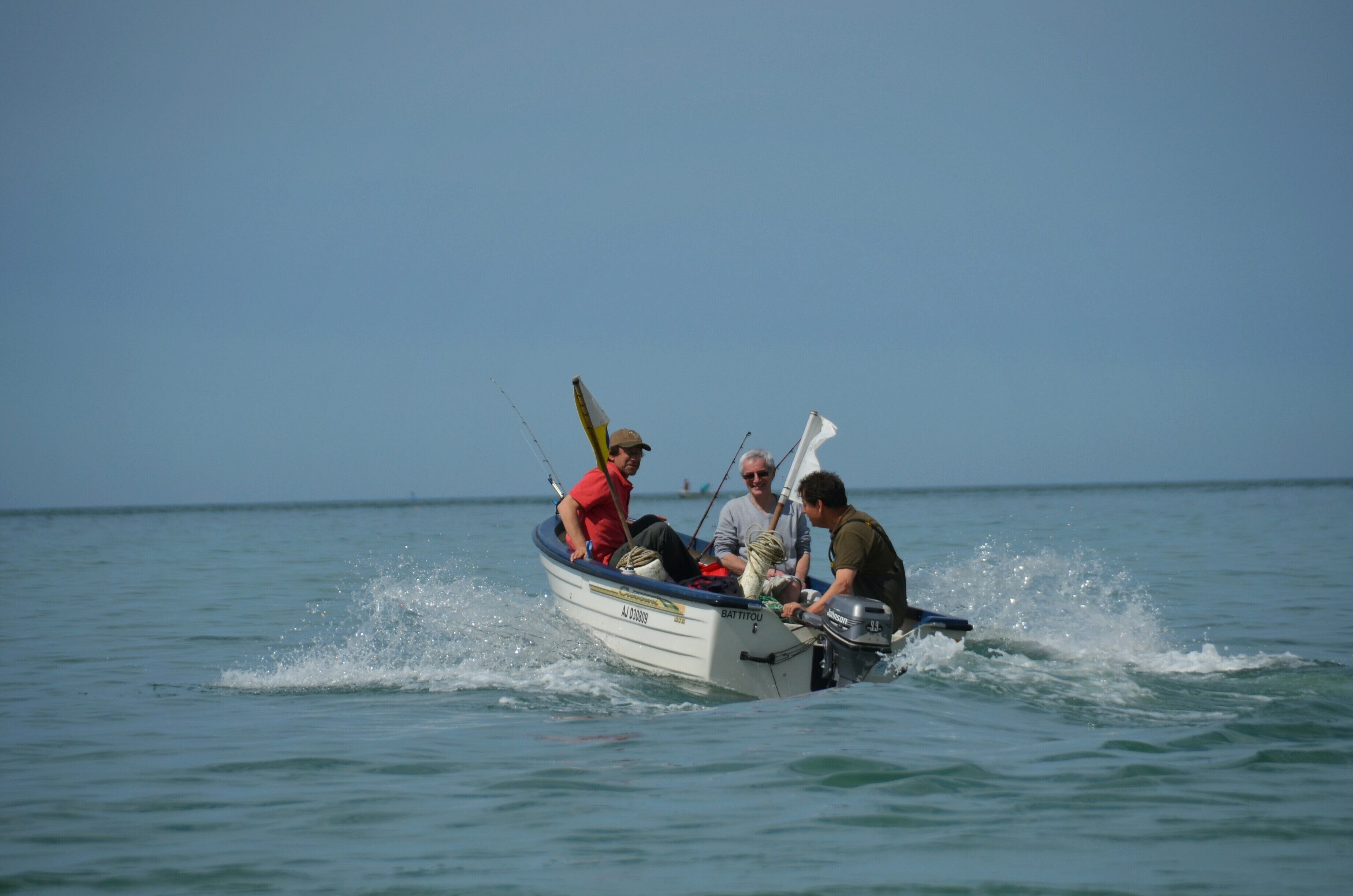 A small boat with three people on it, moving through calm water.