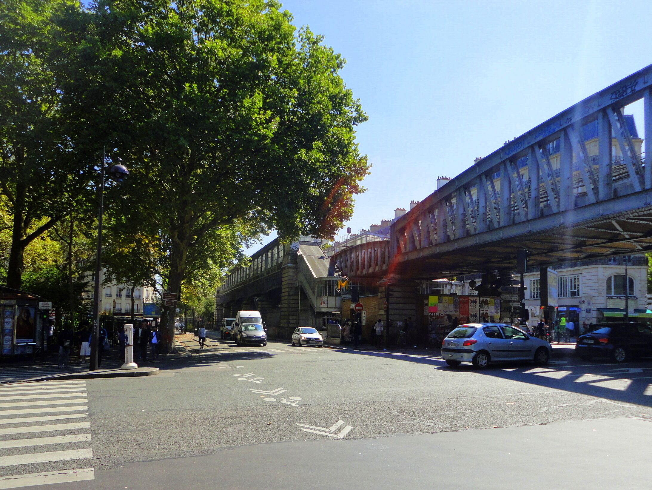 A street intersection with a pedestrian crossing, a tram line, and buildings with signage.