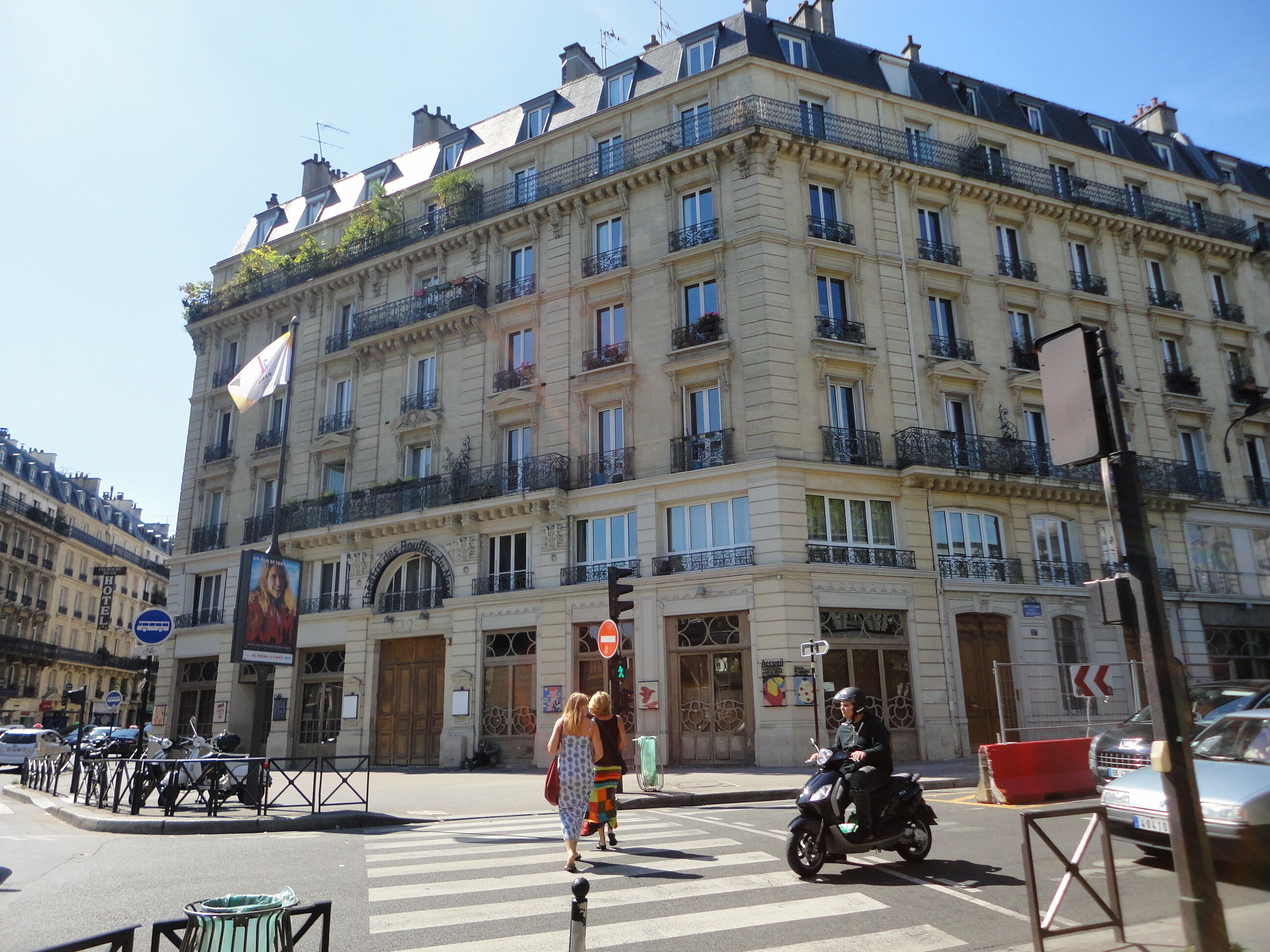 Un edificio de varios pisos con balcones, un cartel de hotel y un paso de peatones.