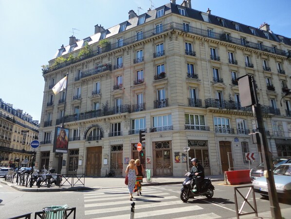 A multi-story building with balconies, a sign for a hotel, and a pedestrian crossing.