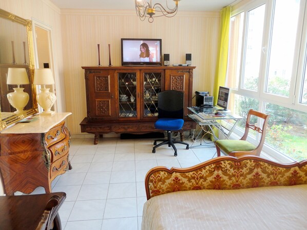 A bedroom with a bed, a desk with a computer, a chair, a dresser, a mirror, and a television.