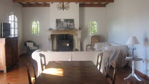 A dining area with a wooden table, chairs, a fireplace, and a television on a cabinet. - villa, countryside, quiet, spacious (8 persons), secure swimming pool. (Sérignan-Du-Comtat)