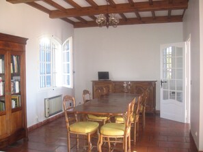A dining room with a wooden table, chairs, a bookshelf, and a door. - villa, countryside, quiet, spacious (8 persons), secure swimming pool. (Sérignan-Du-Comtat)