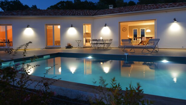 A swimming pool with a sunken seating area, surrounded by a white building with multiple doors and windows. - New villa with swimming pool overlooking a hectare of land overlooking the vineyard (Patrimonio)