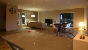 A modern living room with a sofa, TV, dining area, and a large window. - New villa with swimming pool overlooking a hectare of land overlooking the vineyard (Patrimonio)
