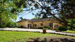 Una casa de dues plantes amb teulada de rajola, façana de pedra i jardí ben cuidat.