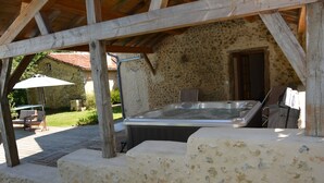 Edifici de pedra amb un bany d'hidromassatge sota una pérgola de fusta.