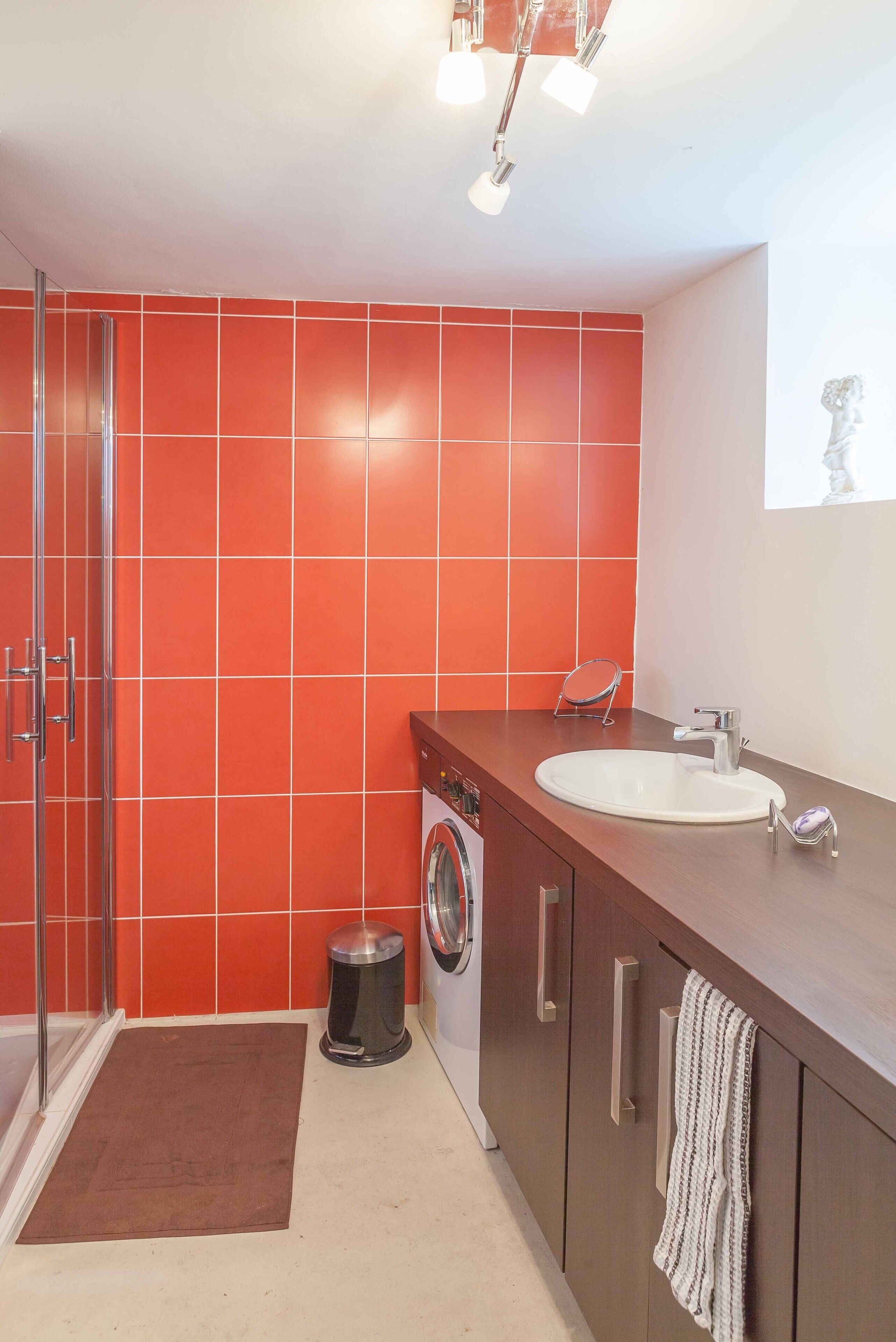 Un bagno moderno con cabina doccia in vetro, lavatrice integrata e mobile lavabo con lavandino e portasciugamani.