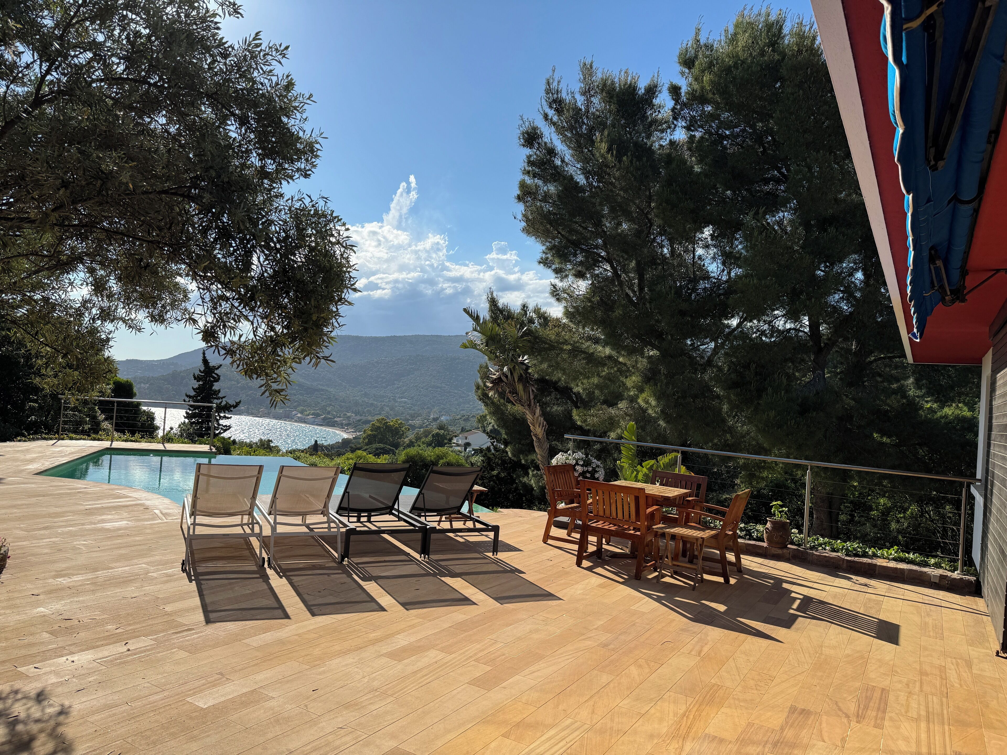 Eine Holzterrasse mit Pool, Liegestühlen und einem Tisch mit Stühlen.