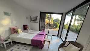A bedroom with two beds, a small table, a chair, and a large window.