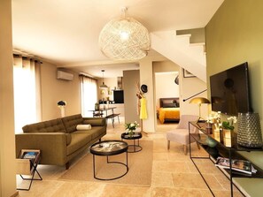 A modern living room with a sofa, coffee table, TV, and a dining area.
