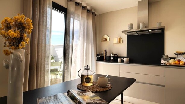 A modern kitchen with a coffee maker, a cup, and a magazine on a table.