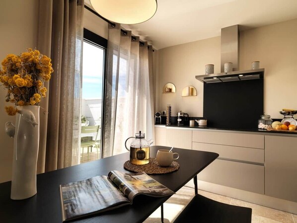 A modern kitchen with a coffee maker, a cup, and a magazine on a table.