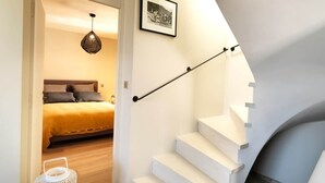 A staircase with white steps leading to a landing, a bed with a yellow blanket, and a hanging light fixture.
