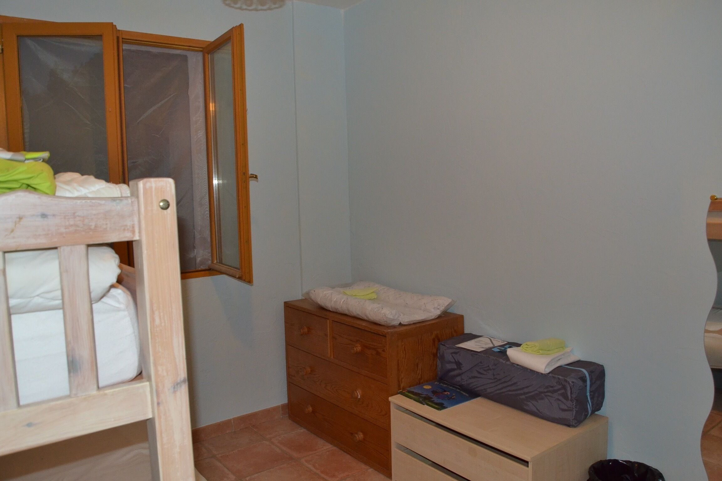 A bedroom with a wooden bed, a dresser, and a small table with a bag and a pillow.