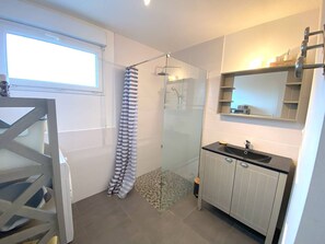 A modern bathroom with a glass shower enclosure, a white vanity with a black countertop, and a window providing natural light. - New Single-Story Home 100m from the Sea, Near Coz-Pors Beach, 3* Comfort with WiFi and Parking (Trégastel)