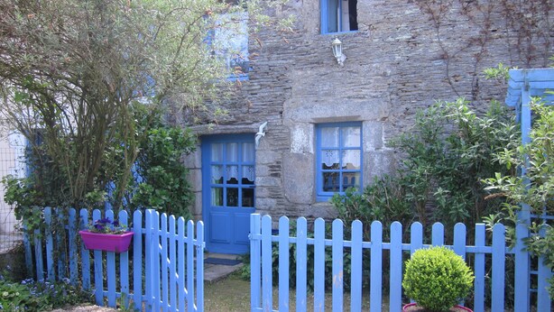 A stone building with blue doors and windows, a picket fence, and potted plants.