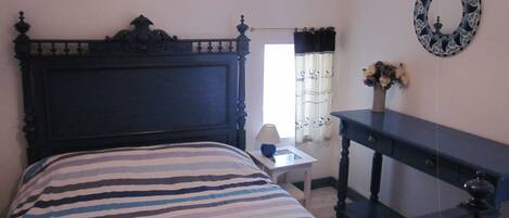A bedroom with a dark wooden bed, a bedside table with a lamp, a small desk, and a decorative mirror on the wall.