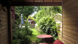 A wooden room with a red sofa and a small table. There is a view of a garden with a wooden fence and a wooden deck.