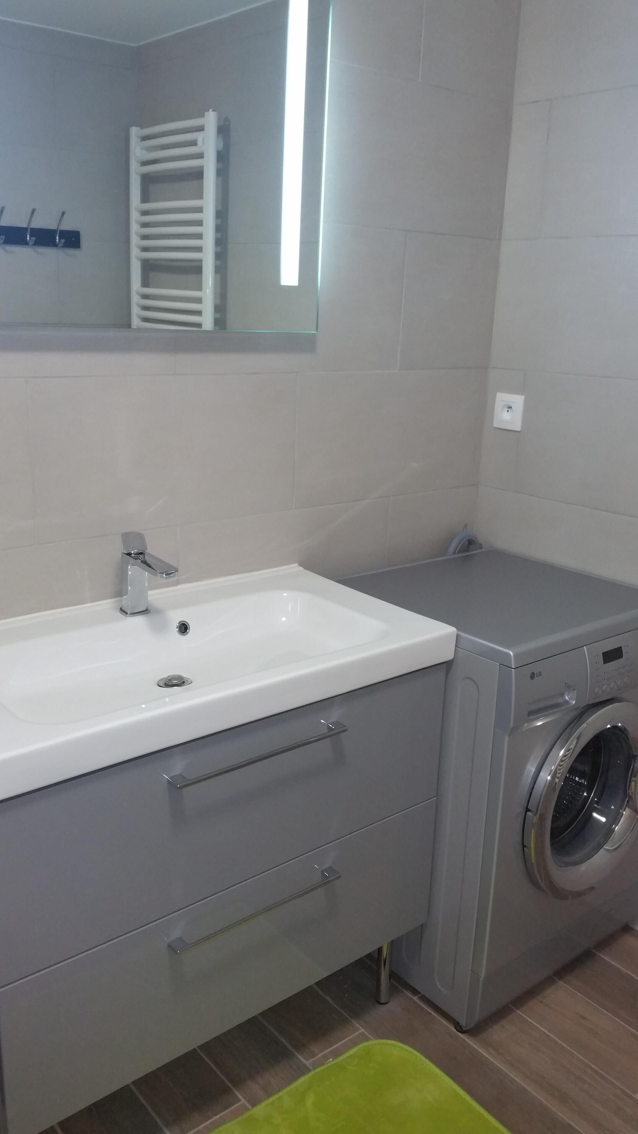 Une salle de bain moderne avec un lavabo blanc, des meubles gris et un lave-linge à chargement frontal.