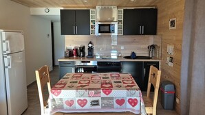 Une cuisine compacte avec des meubles en bois, un four à micro-ondes, une machine à café et une table recouverte d’une nappe à motifs en forme de cœur.